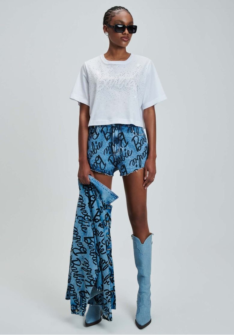 Modelo-usando-short-jeans-azul-estampado-Barbie-de-cintura-alta-com-camiseta-branca-cropped-oculos-escuros-e-bota-azul-de-cano-alto