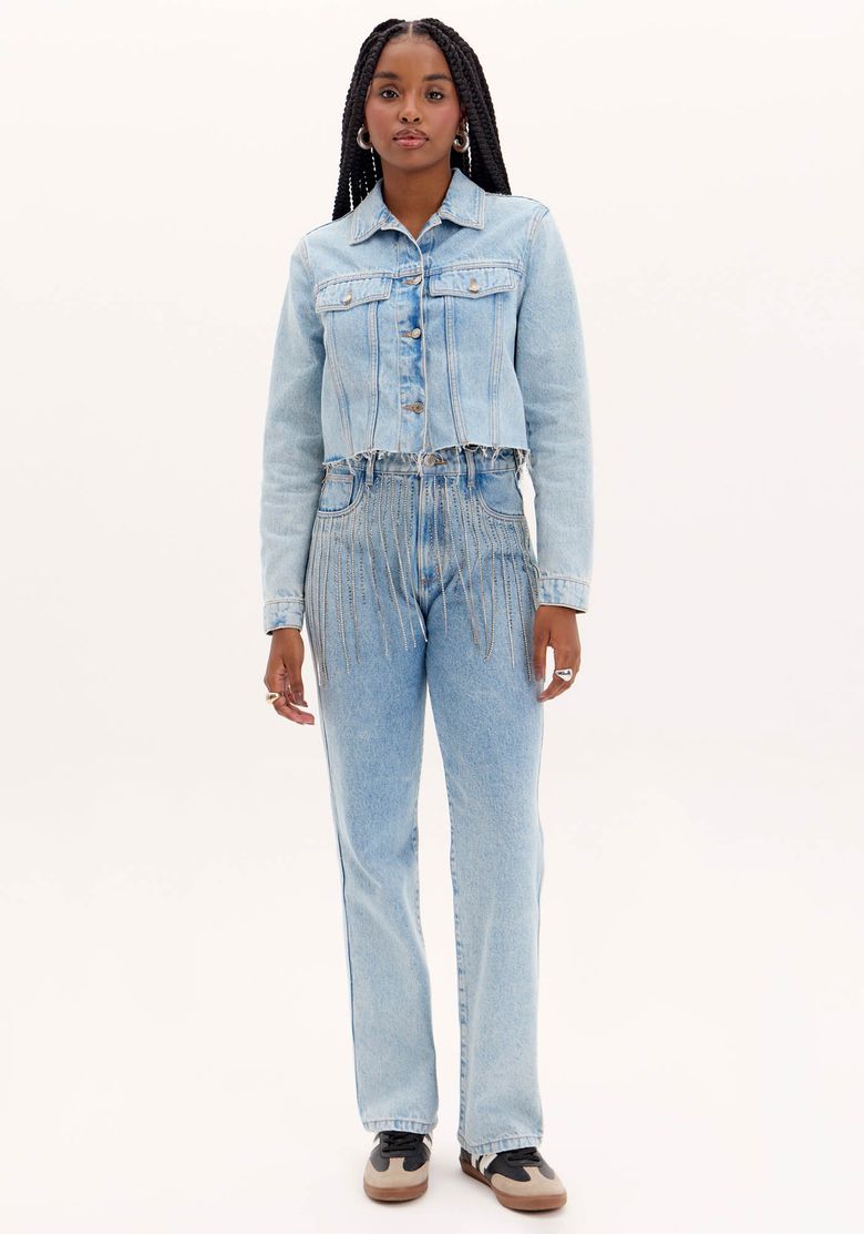 Modelo em corpo inteiro usando calça jeans reta cintura alta azul claro com franjas de brilhos no cós, vista frontal