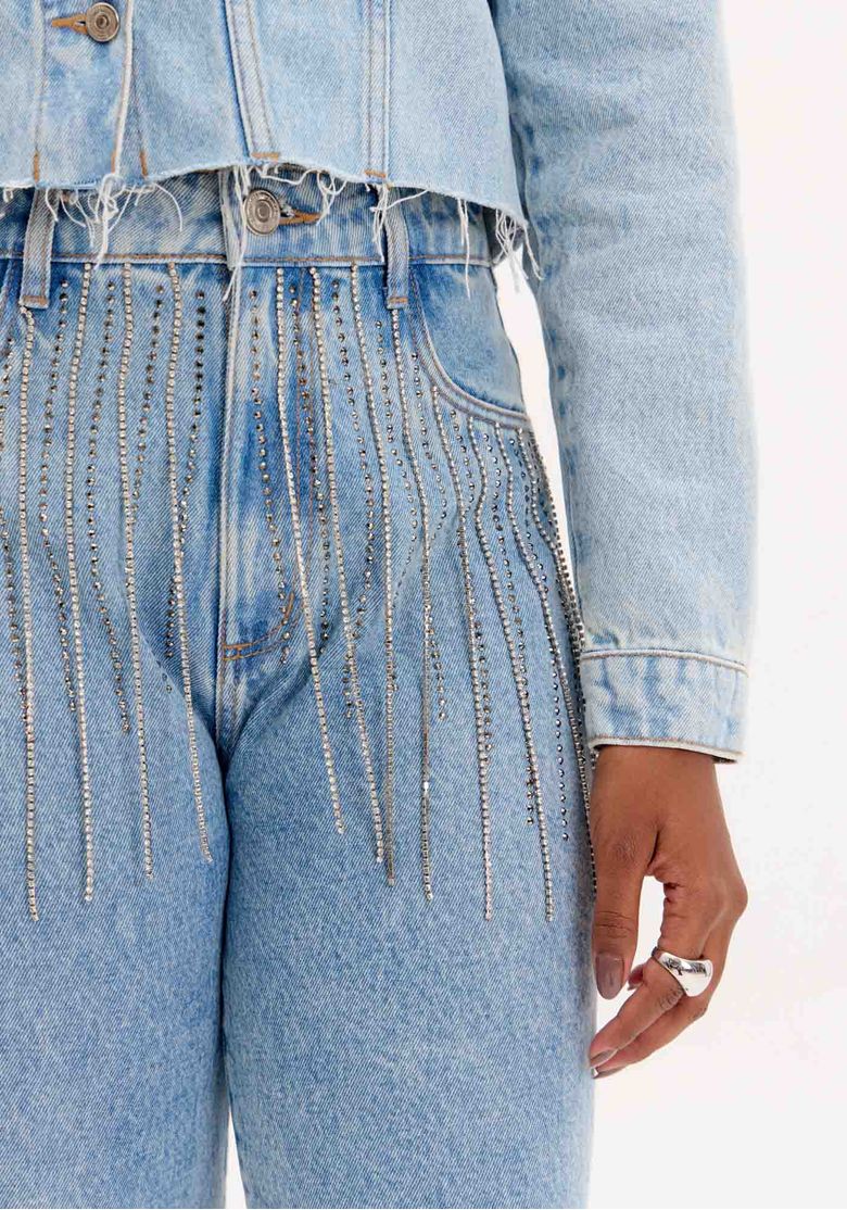 Modelo de costas mostrando calça jeans reta azul claro com bolsos traseiros chapados e aplicação de brilho na cintura, vista posterior