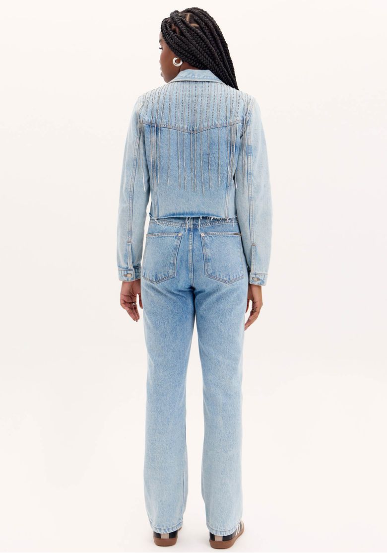 Close no cós frontal da calça jeans azul claro com aplicação de franjas de strass pendentes e passantes para cinto, detalhe do acabamento