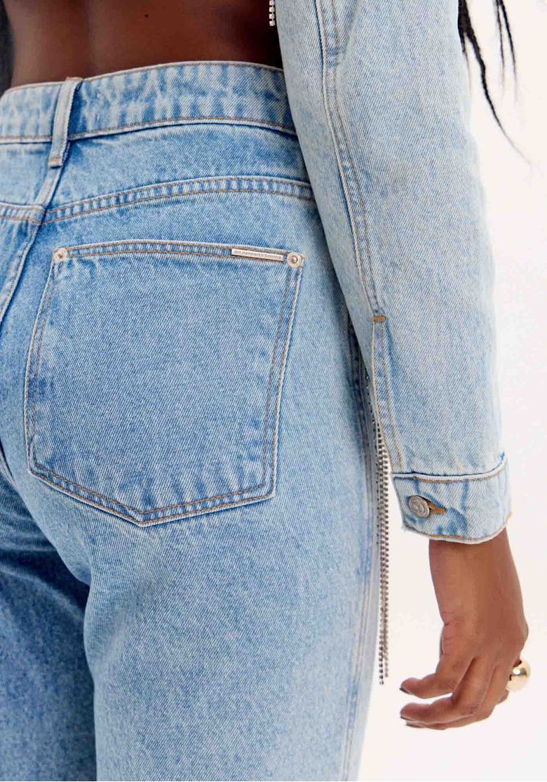 Close do bolso traseiro da calça jeans reta azul claro evidenciando costura e textura do denim