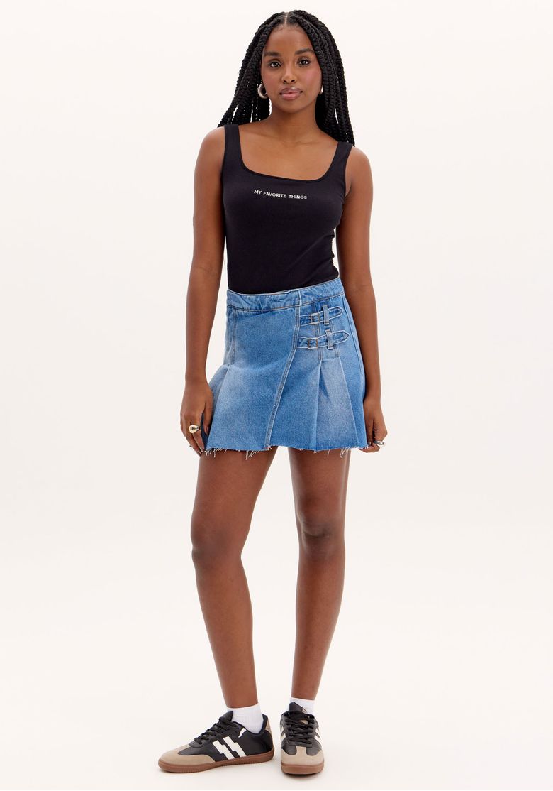 Modelo vestindo saia curta jeans com fivelas laterais e top preto, vista frontal.