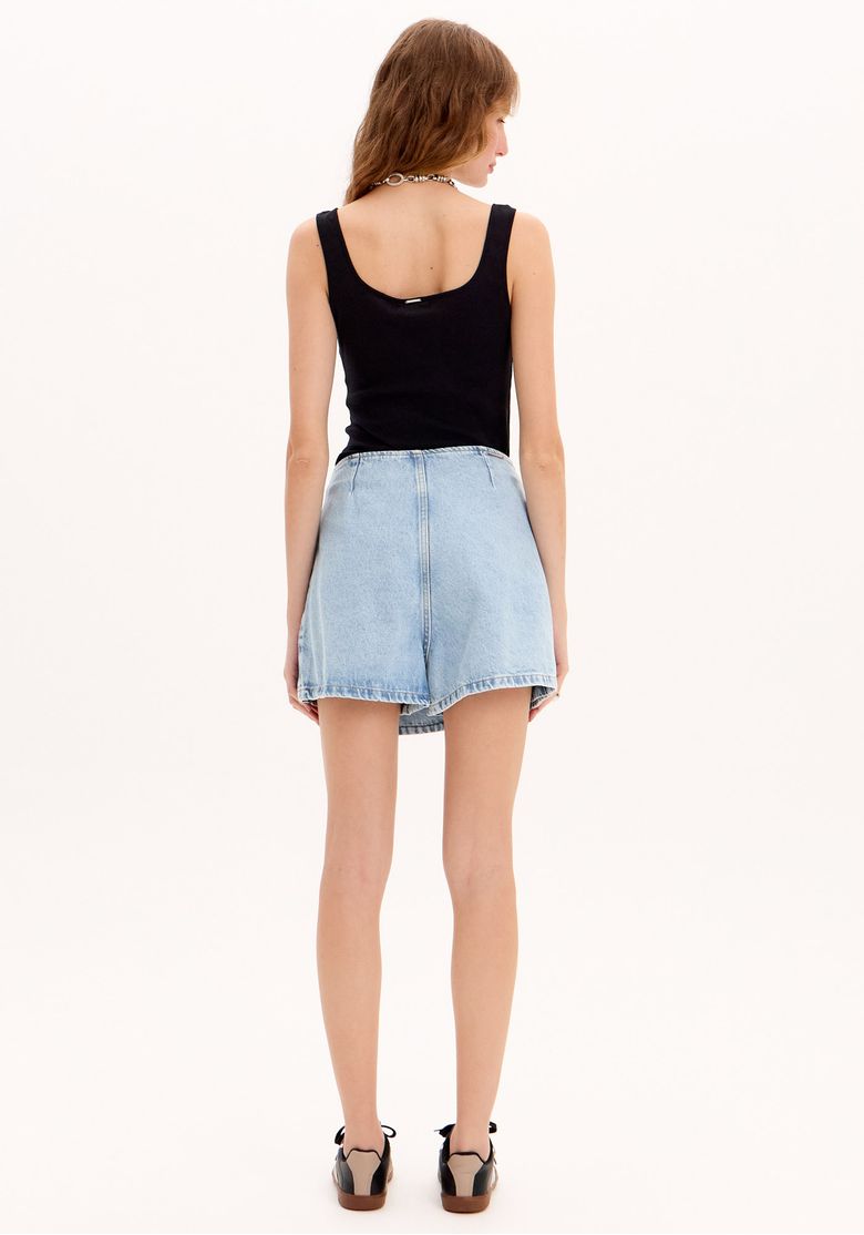 Detalhe da cintura do short saia jeans com sobreposição frontal, botão lateral e costura visível em lavagem clara.