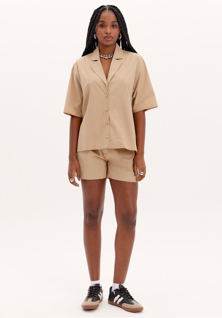 Modelo vestindo bermuda de alfaiataria bege com camisa combinando, vista frontal.