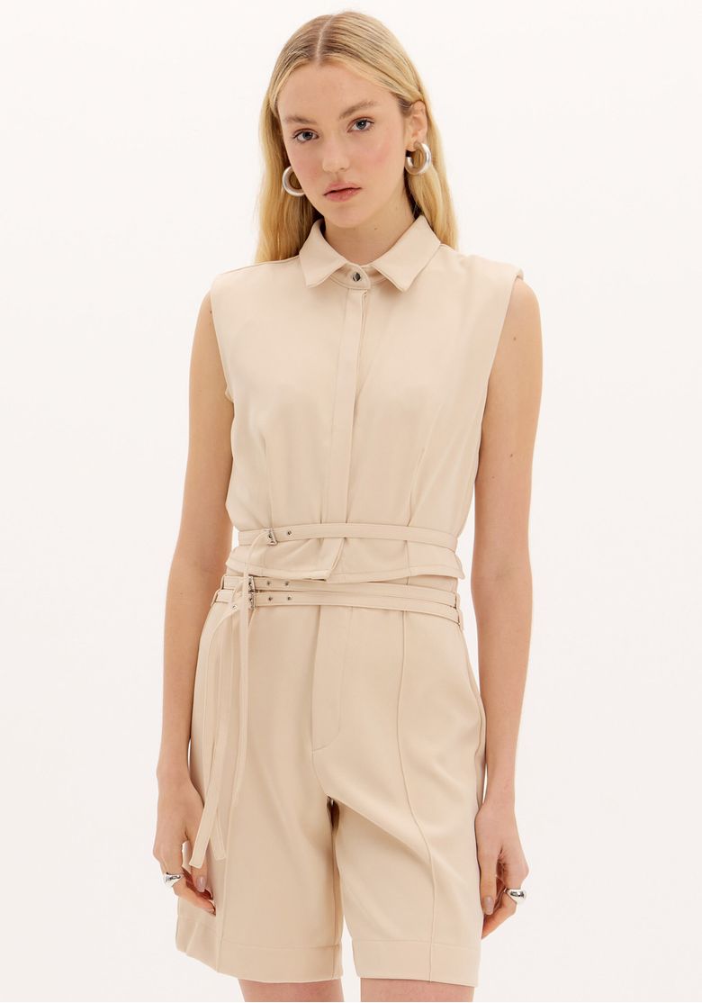 Modelo usando camisa cropped bege sem manga com cinto e short de alfaiataria, look feminino moderno e elegante