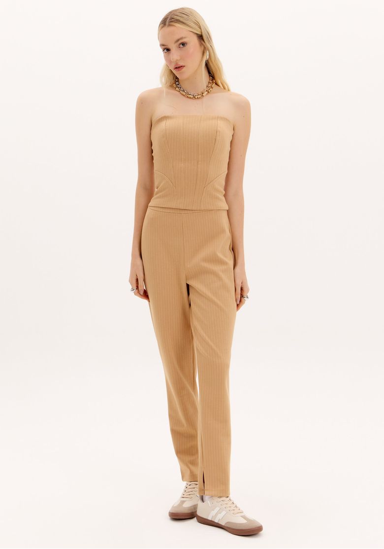 Modelo usando calça carrot risca de giz bege de cintura alta com caimento afunilado e comprimento longo em look feminino elegante