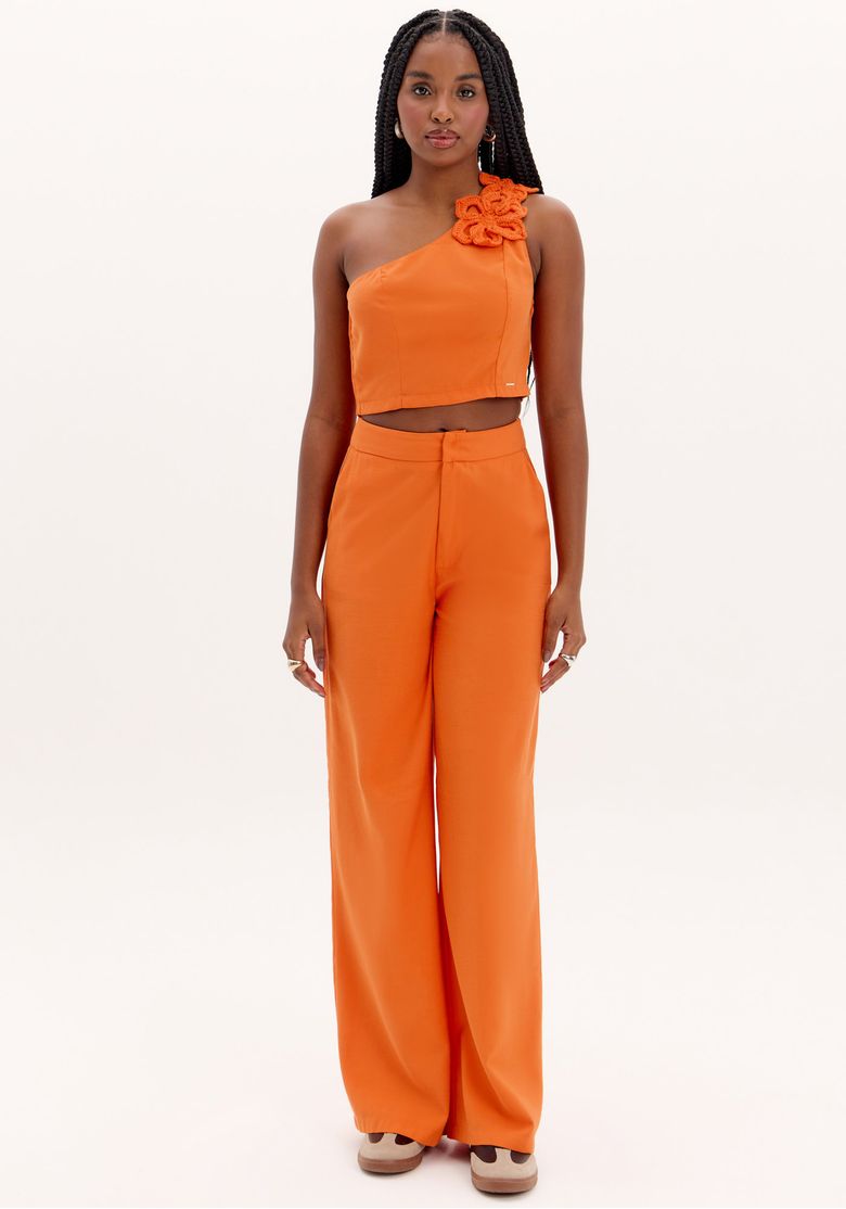 Modelo em pé usando calça wide leg laranja cintura alta em alfaiataria, vista frontal mostrando caimento longo e perna ampla