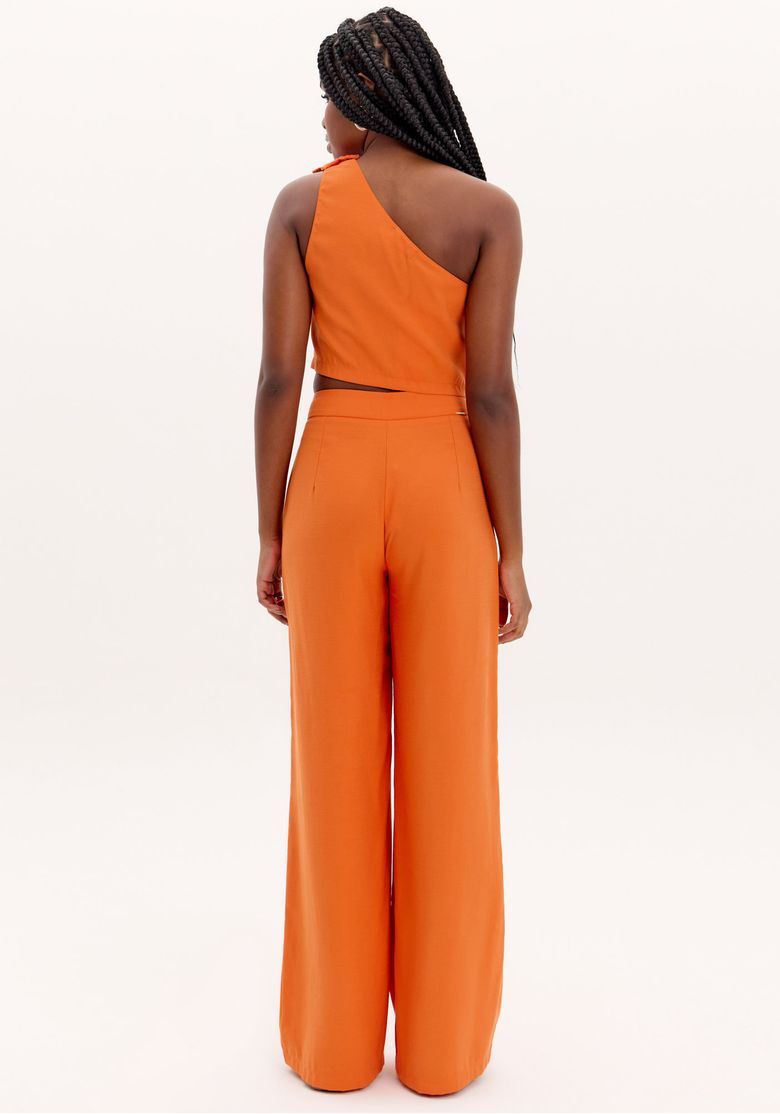 Close frontal da calça wide leg laranja mostrando cós estruturado, fechamento discreto e tecido plano leve com drape suave