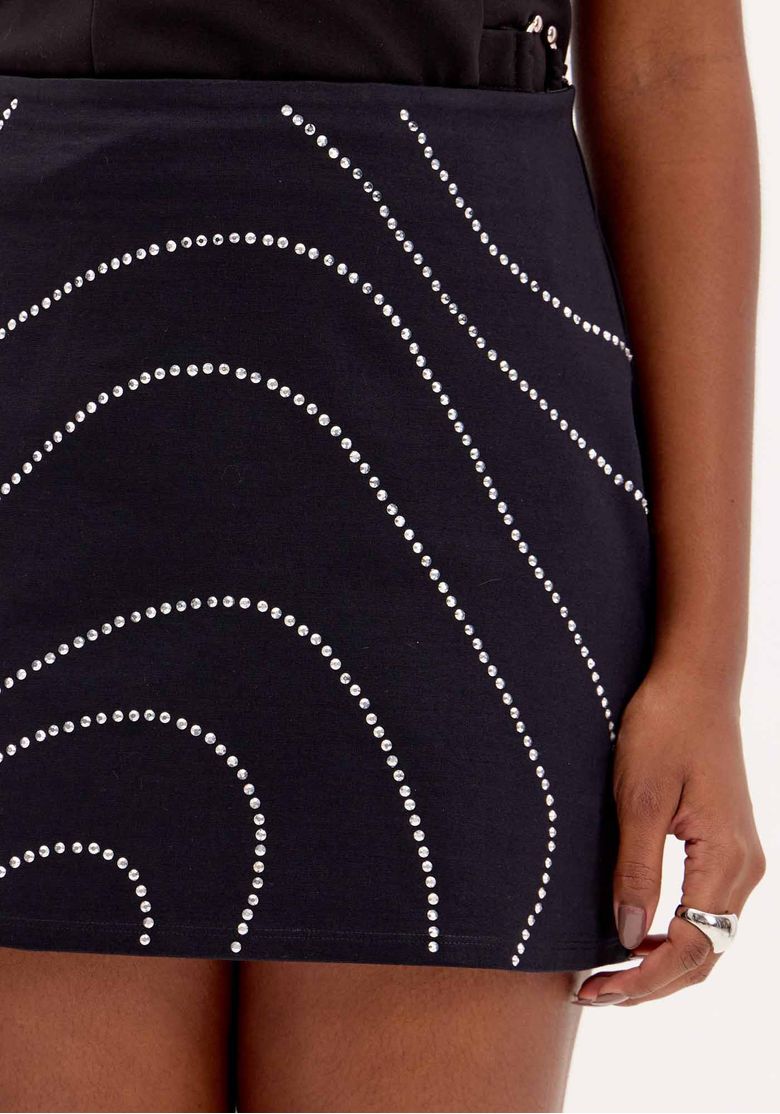 Close da saia curta preta com aplicações de brilho em linhas curvas, detalhe frontal da mini saia ajustada feminina