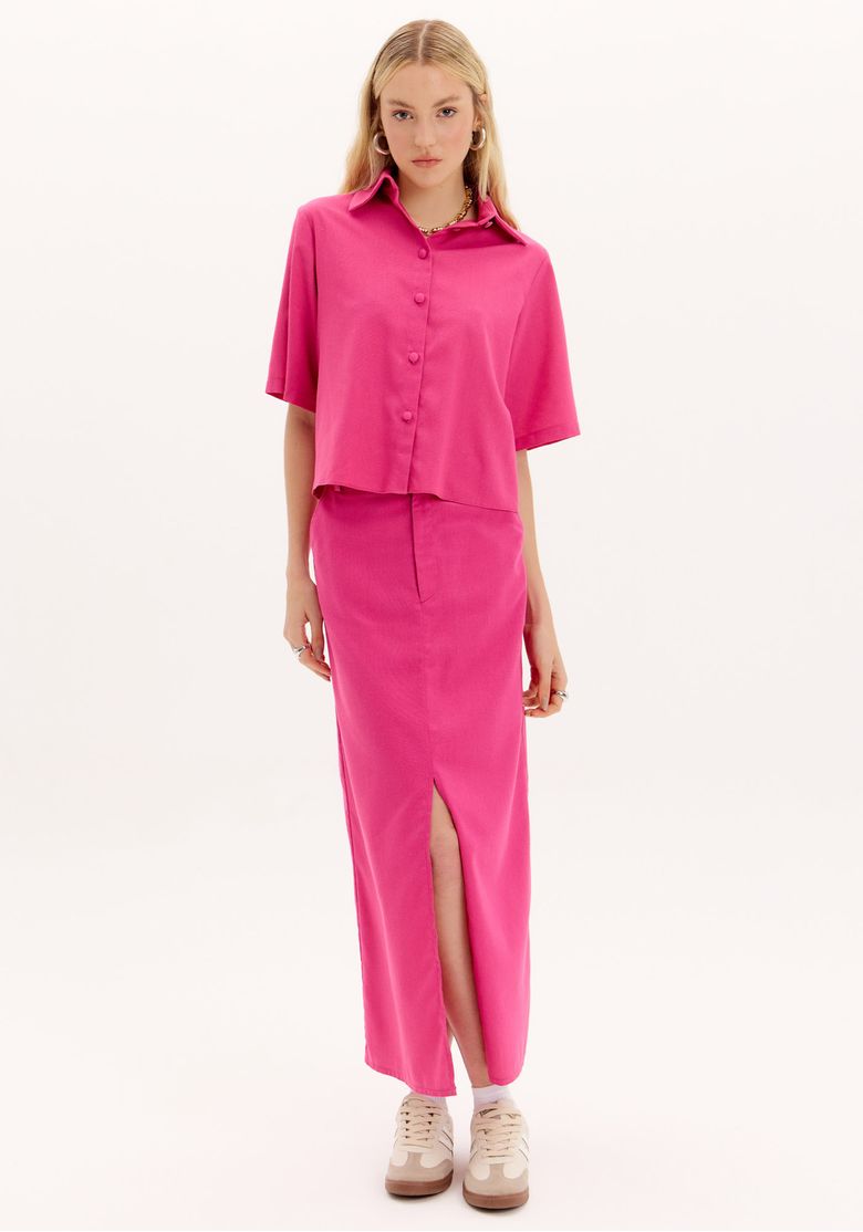 Modelo em estúdio usando saia midi alfaiataria rosa com fenda frontal e camisa cropped rosa, vista frontal completa mostrando cintura alta e caimento reto