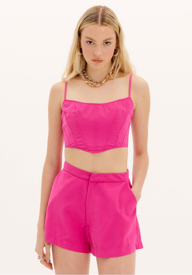 Top cropped corset rosa vista frontal em modelo, top cropped acinturado com alças finas reguláveis e recortes estruturados, look coordenado com shorts rosa