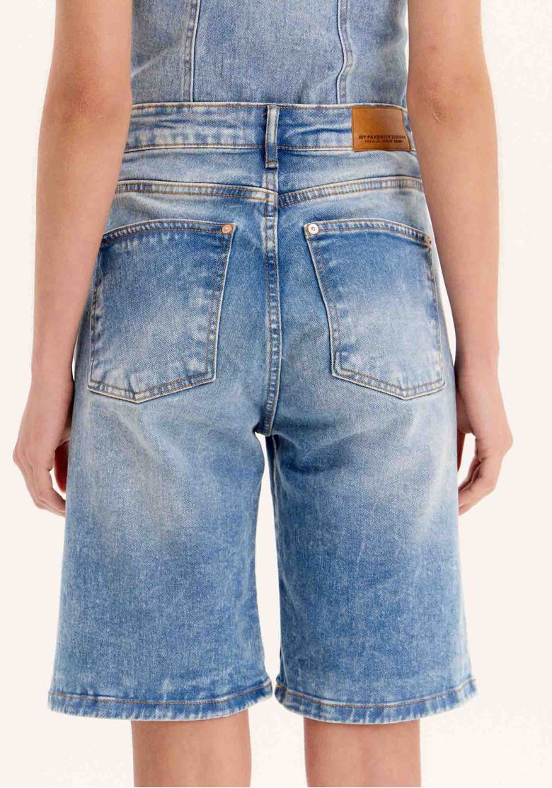 Close traseiro da bermuda jeans com detalhe de etiqueta na cintura, costura e acabamento da barra - detalhe costas bermuda jeans