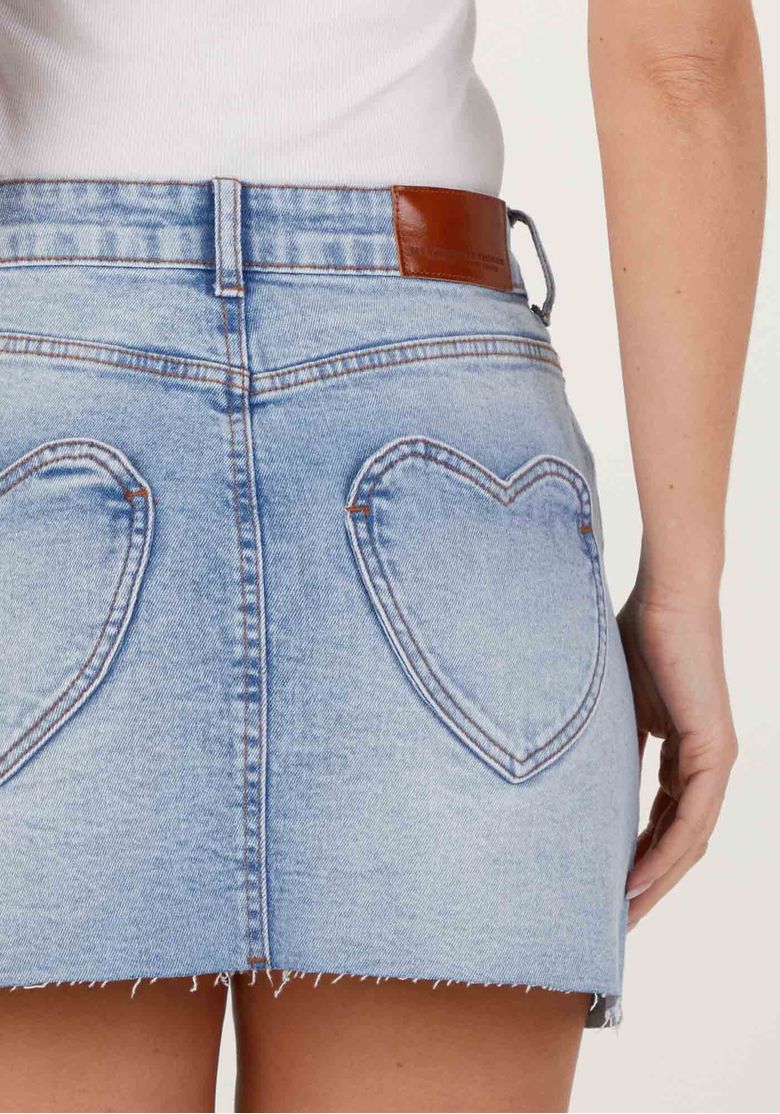 Detalhe dos bolsos traseiros em formato de coração na saia jeans azul e etiqueta de couro no cós, destacando costura e lavagem