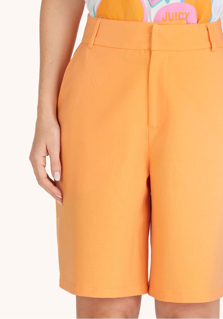 Vista traseira da bermuda laranja em modelo com camiseta branca mostrando bolsos e caimento na parte de trás
