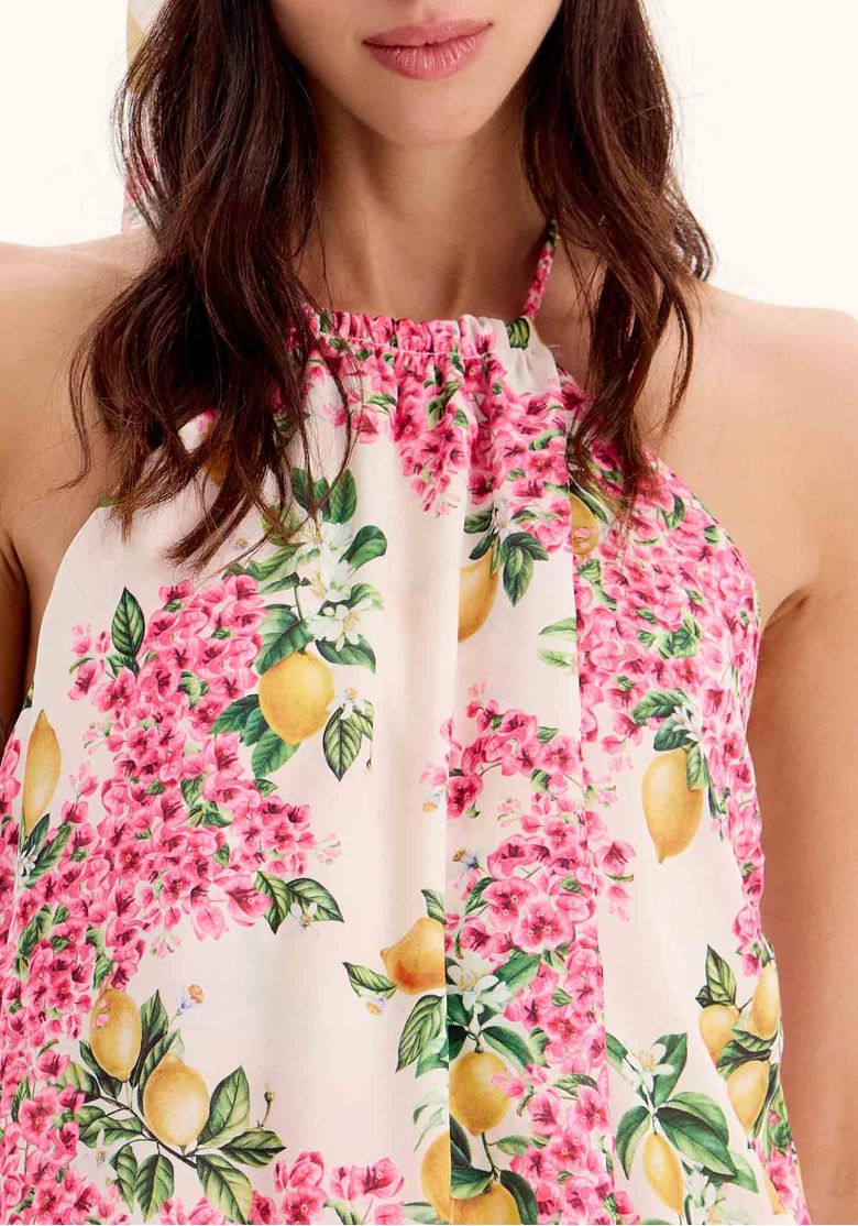 Close da blusa estampada feminina com gola alta franzida, estampa floral rosa e limões em fundo bege