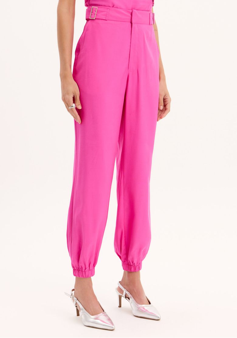 Detalhe do cós com fivelas e tecido rosa vibrante da calça jogging.