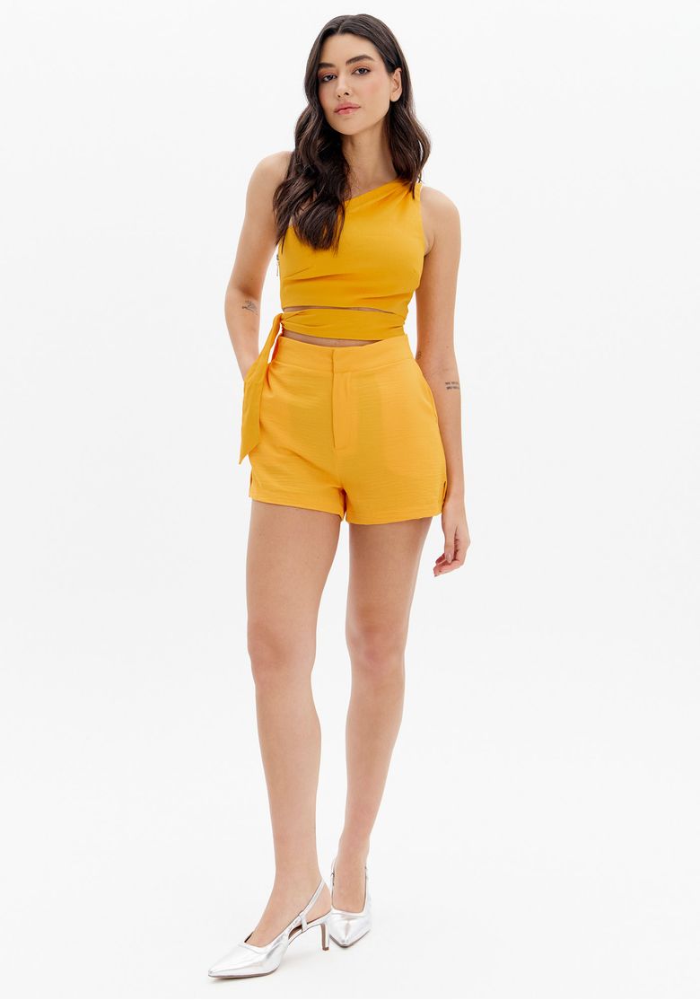 Modelo vestindo short laranja com cintura alta e top assimétrico, vista frontal.