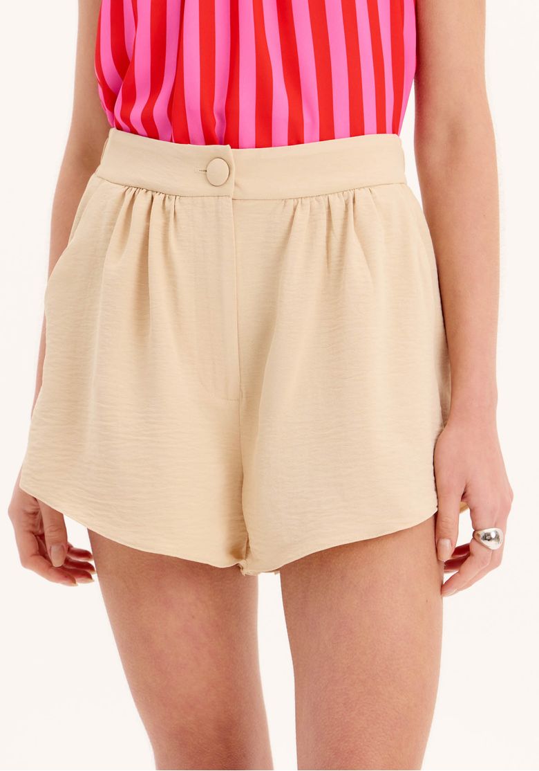 Detalhe do cós e fechamento do short boxer de alfaiataria bege.
