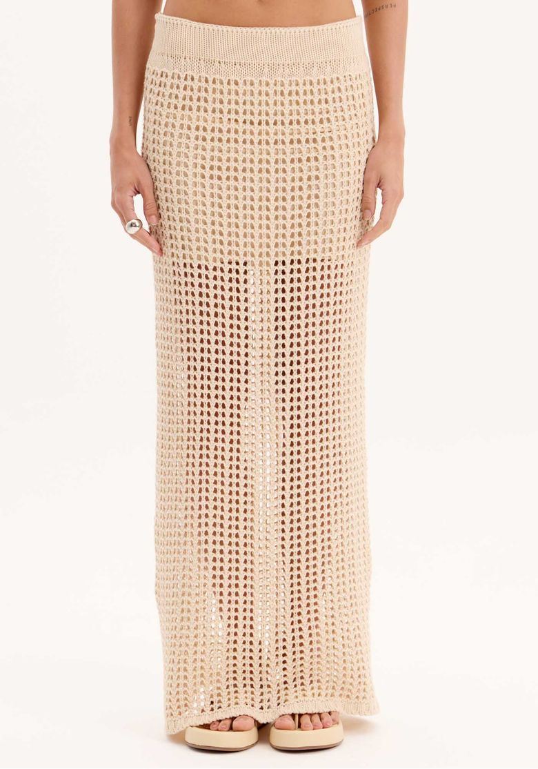 Close frontal da saia longa de tricot bege com cintura alta, trama aberta e fenda frontal, ideal para look sofisticado de verão