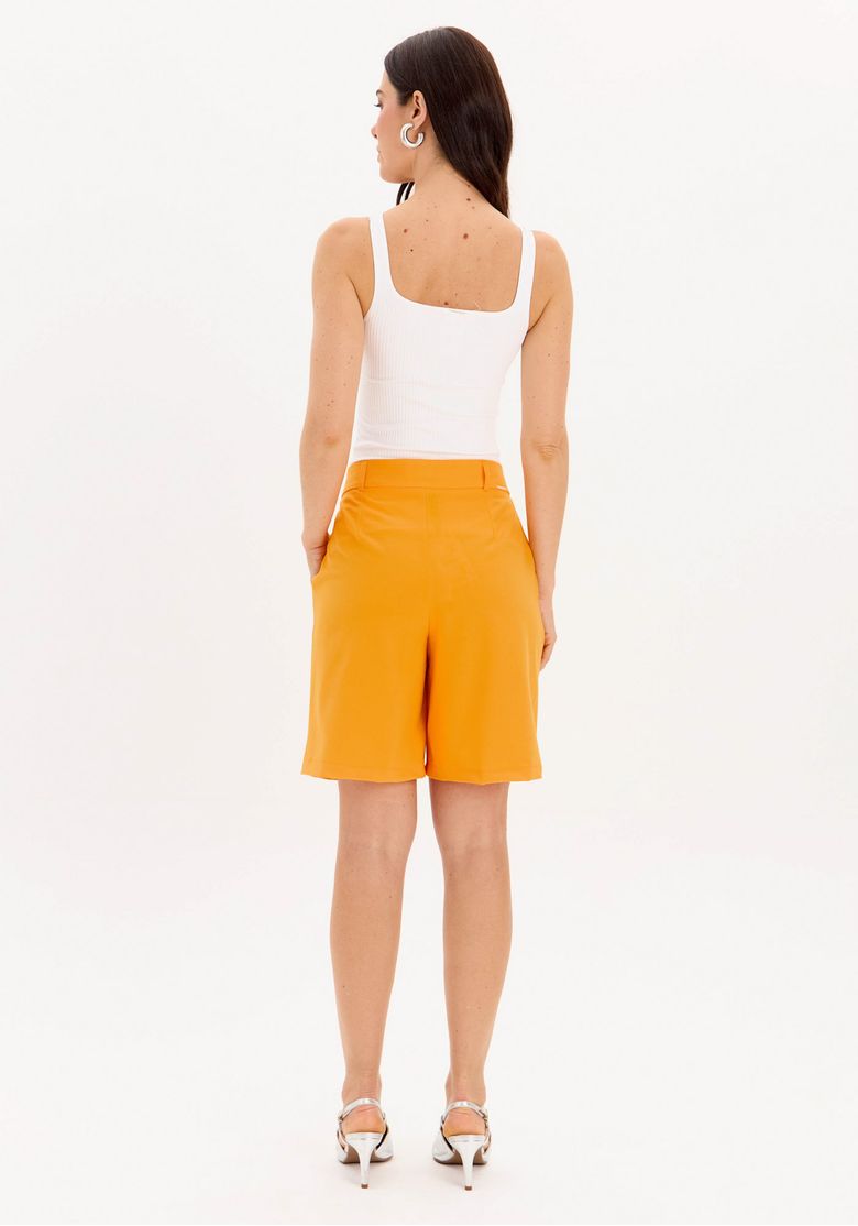 Modelo vista traseira usando bermuda laranja com top regata branco, evidenciando comprimento e barra limpa