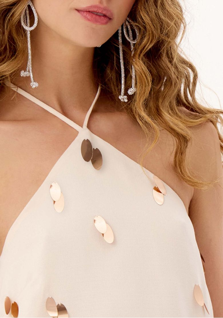 Close da blusa bege assimétrica com aplicações brilhantes e decote halter com amarração fina