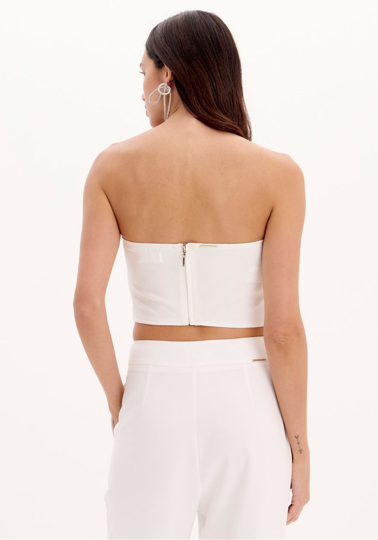 Close frontal da blusa corset branca com franjas de brilho prateado e recortes verticais tipo corset, destaque no acabamento em brilho