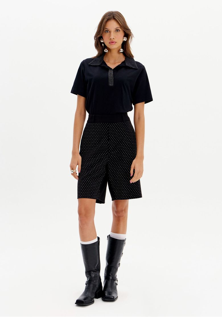 Modelo vestindo bermuda alfaiataria preta com brilhos, combinada com camisa preta e botas.