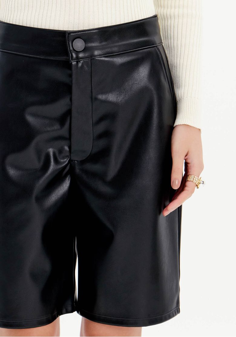Close da bermuda de PU preta feminina com cintura alta, botão frontal, bolso lateral e acabamento liso acetinado