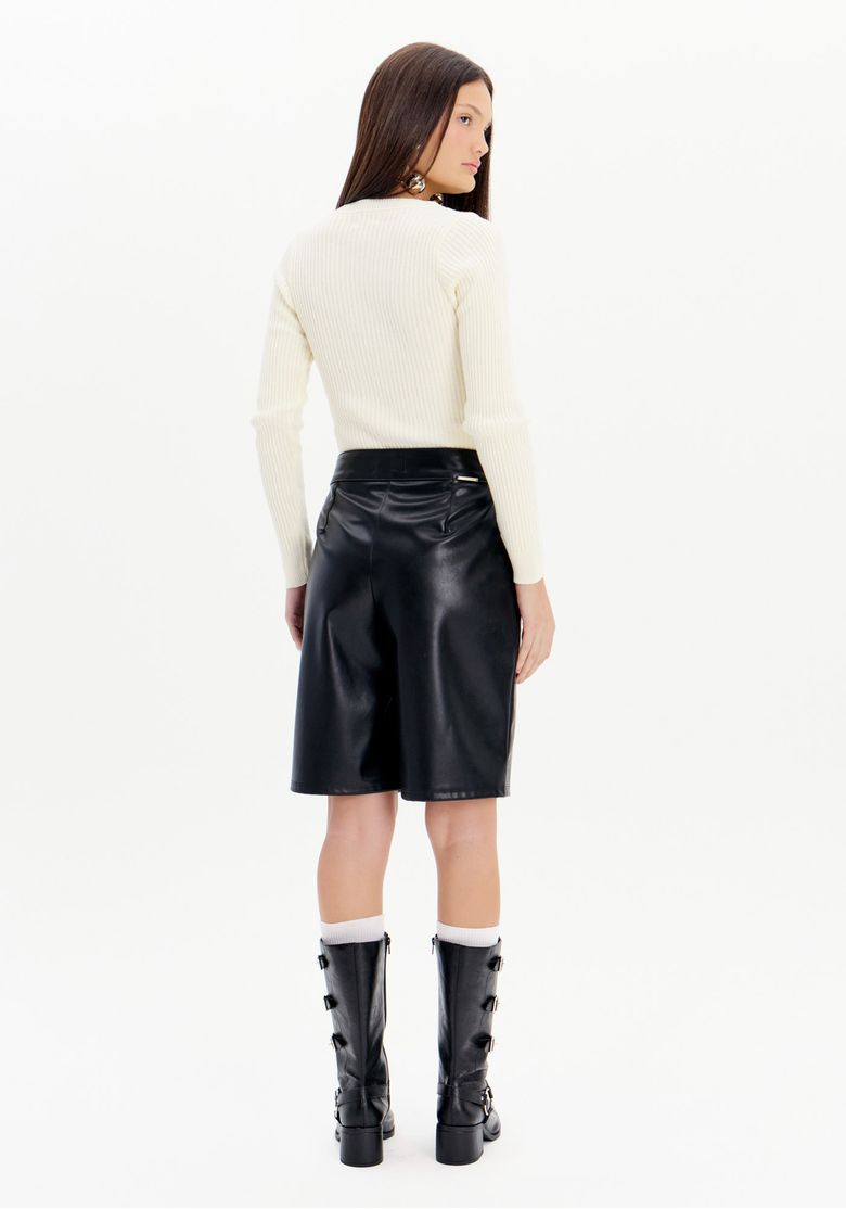 Vista traseira da bermuda de PU preta feminina de comprimento bermuda e caimento reto, usada com blusa de manga longa e botas pretas