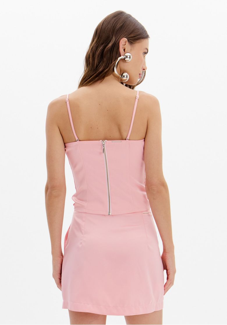 Vista costas da blusa corset rosa com alças finas e fechamento por zíper traseiro, combinada com saia curta rosa