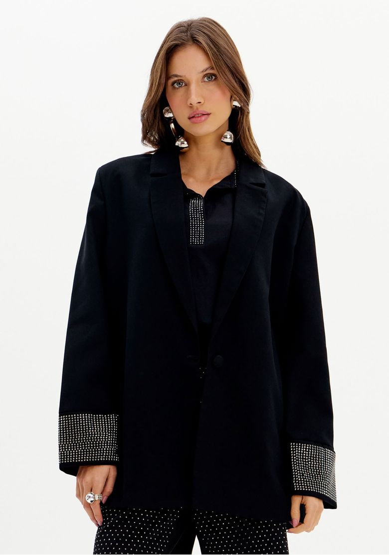 Modelo usando blazer oversized preto de alfaiataria com lapela clássica e aplicações de brilho nos punhos, vista frontal