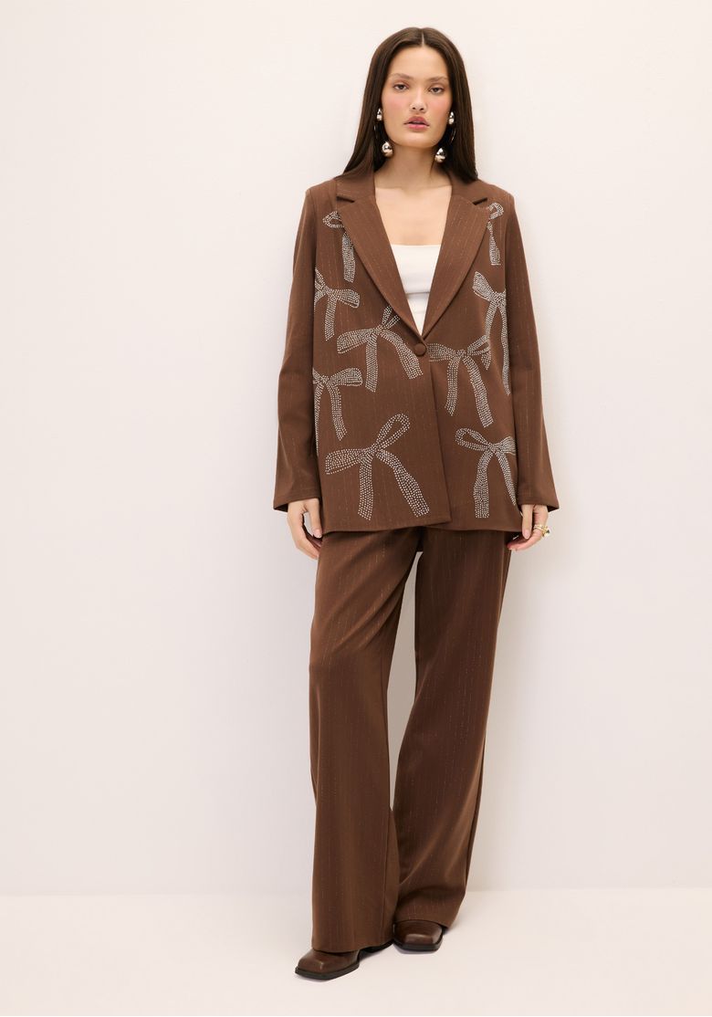 Modelo vestindo calça reta de alfaiataria marrom com riscas de giz, combinada com blazer.