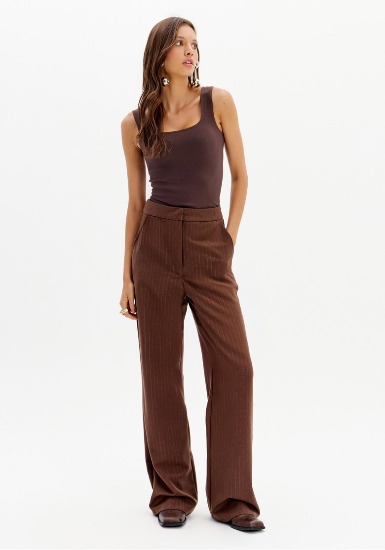 Modelo usando a calça reta de alfaiataria marrom com riscas de giz em um look casual.