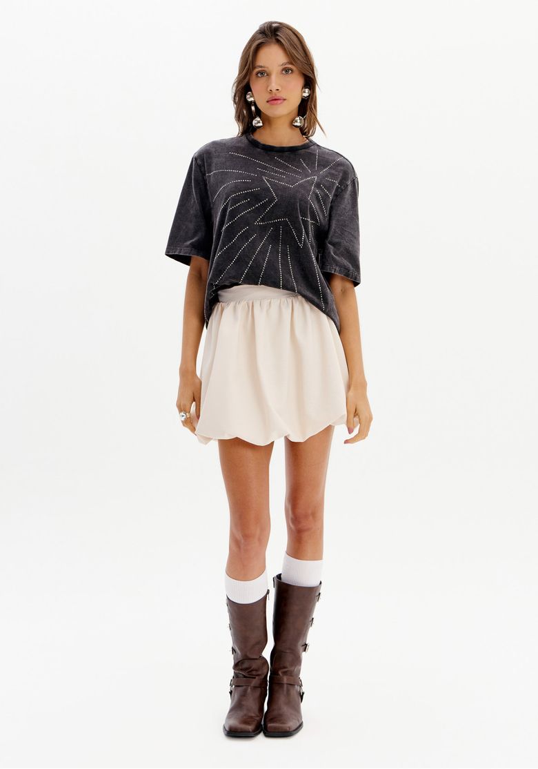 Modelo vestindo saia curta balonê bege com camiseta preta e botas marrons.