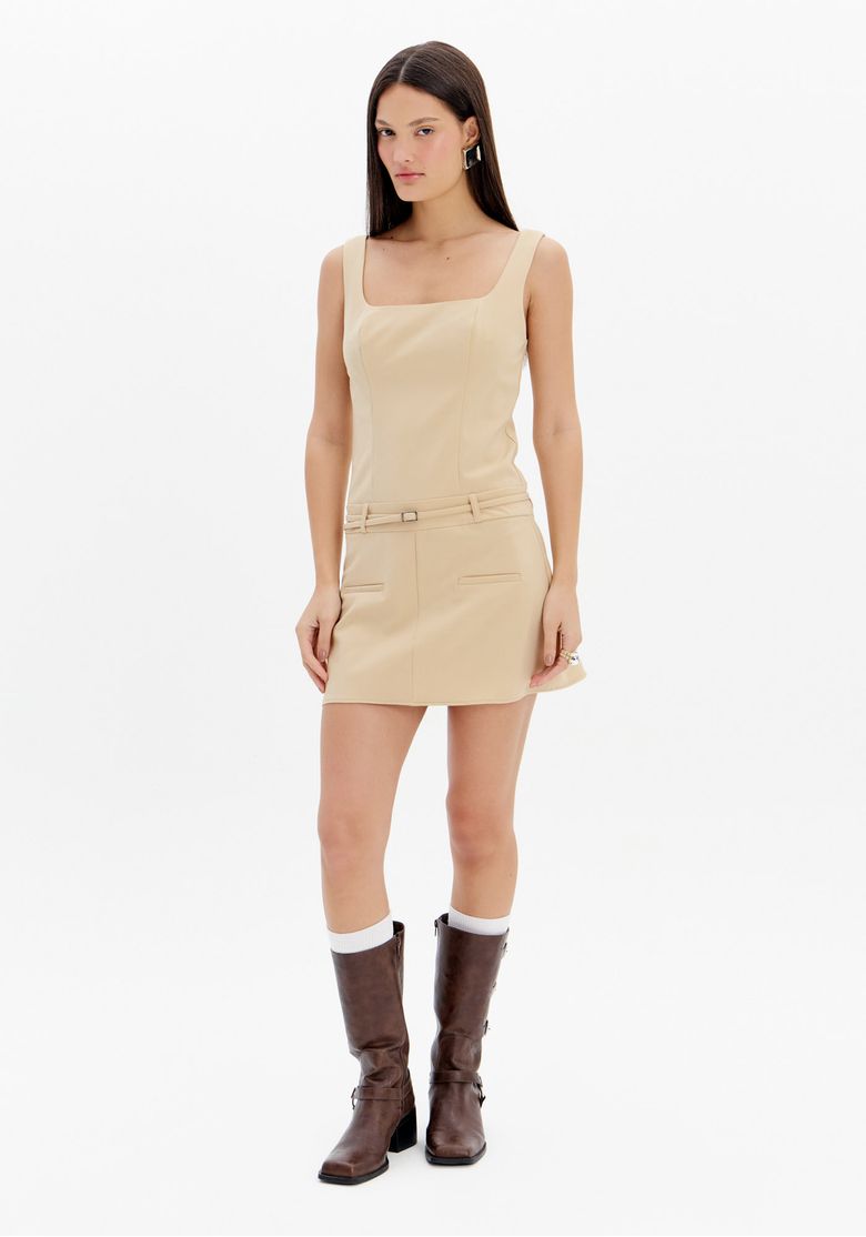 Modelo usando vestido curto de alfaiataria bege com alças largas, cinto fino na cintura e botas de cano médio marrom em look feminino urbano