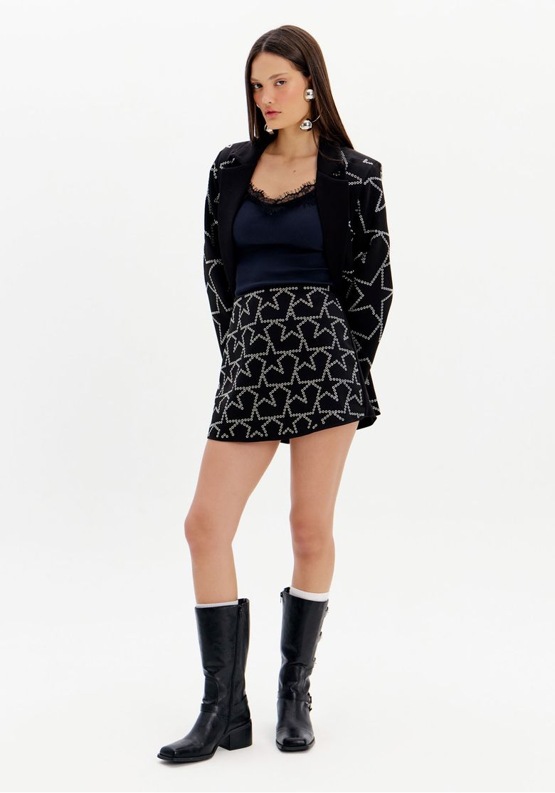 Modelo-vestindo-short-saia-preto-com-estrelas-brilhantes-e-blazer-combinando-botas-pretas.