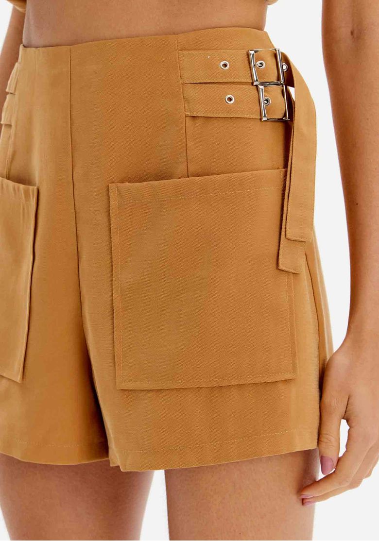 Detalhe lateral do short mostrando as fivelas decorativas e os bolsos.