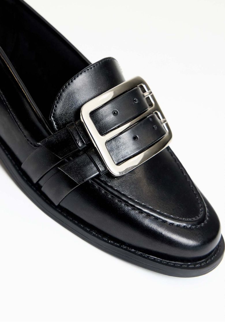 Detalhe da fivela dupla em metal do mocassim preto.