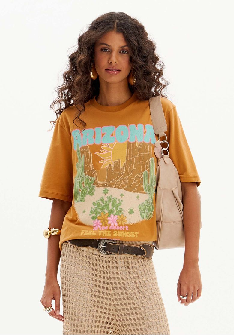 Modelo usando t-shirt oversized feminina marrom com estampa Arizona retrô, manga curta e gola redonda, em look casual urbano