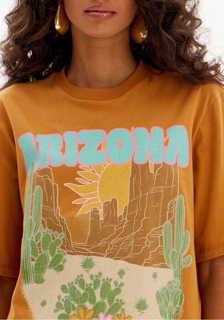 Close da t-shirt oversized marrom com estampa frontal Arizona, paisagem desértica, cactos e tipografia colorida