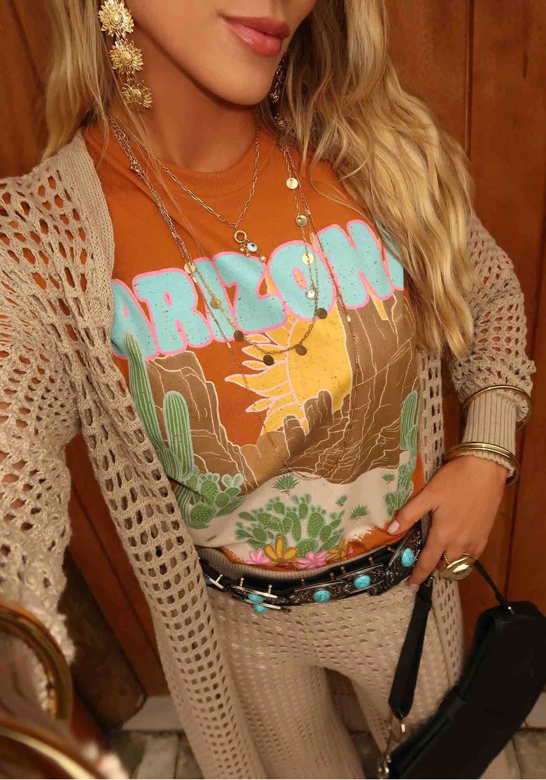 Detalhe de styling da camiseta marrom estampada Arizona com cardigan de tricô vazado bege e acessórios