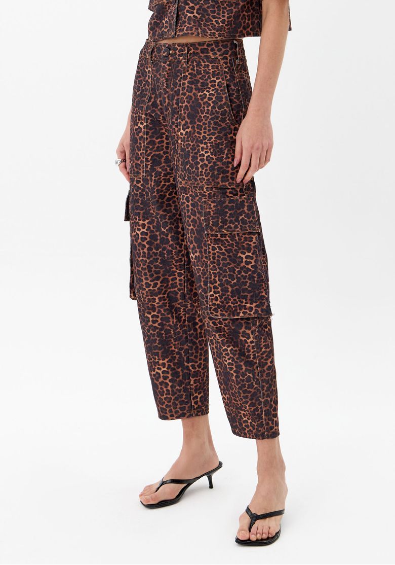 Close lateral da calça cargo animal print feminina de sarja marrom com modelagem baggy, barra reta e sandália de salto baixo