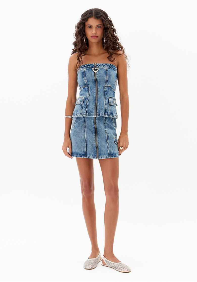 Modelo vestindo saia jeans curta com zíper frontal e lavagem estonada, vista frontal.