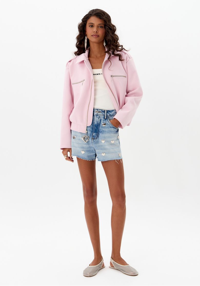Modelo vestindo short jeans grandfather com aplicações de corações metálicos e jaqueta rosa.