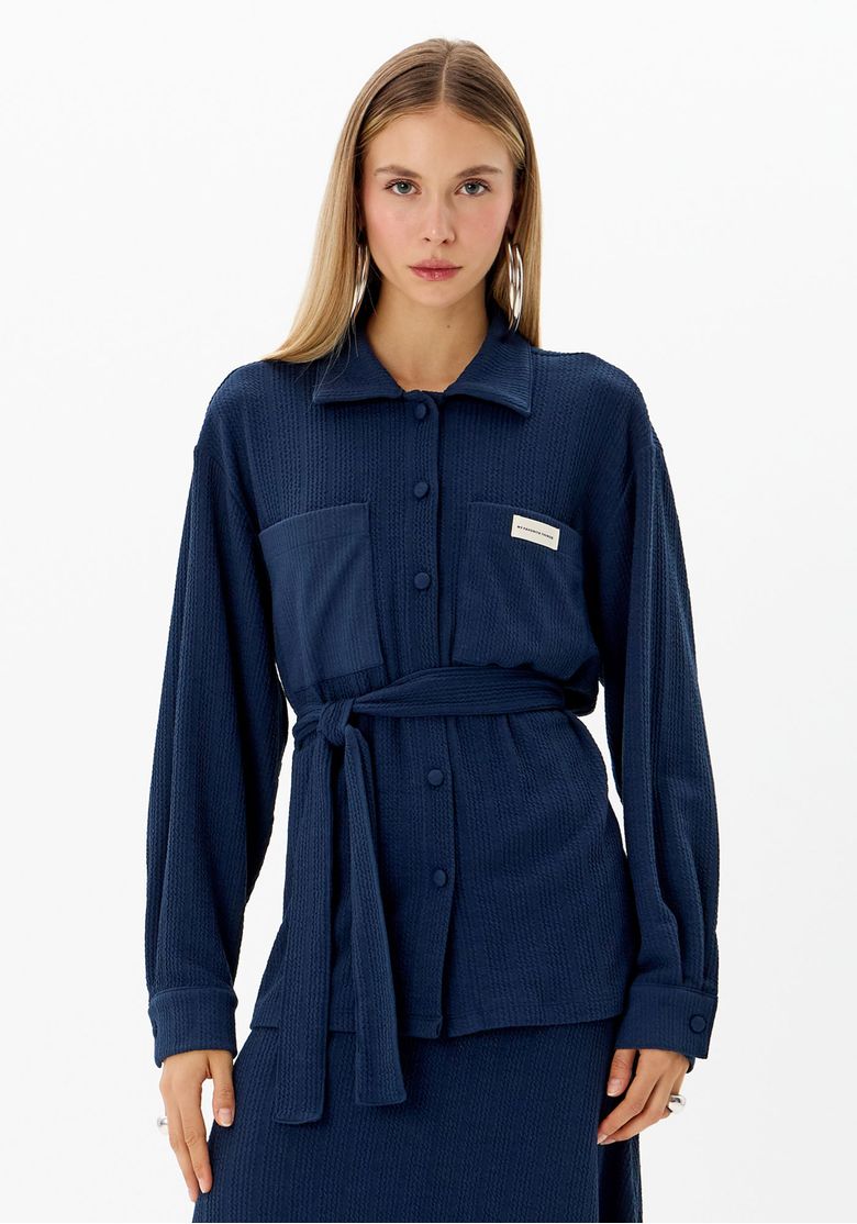 Modelo vestindo camisa alongada azul com faixa ajustável, vista frontal.