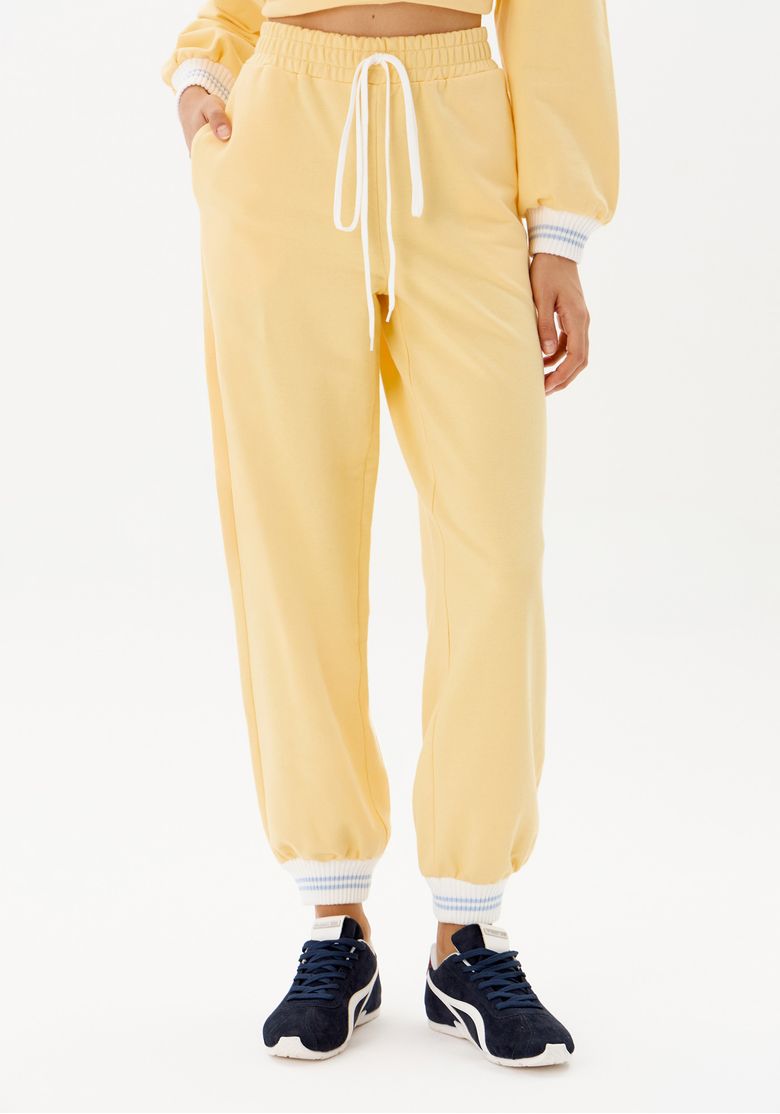 Detalhe do cós elástico com cordão e punhos canelados da calça jogger amarela.