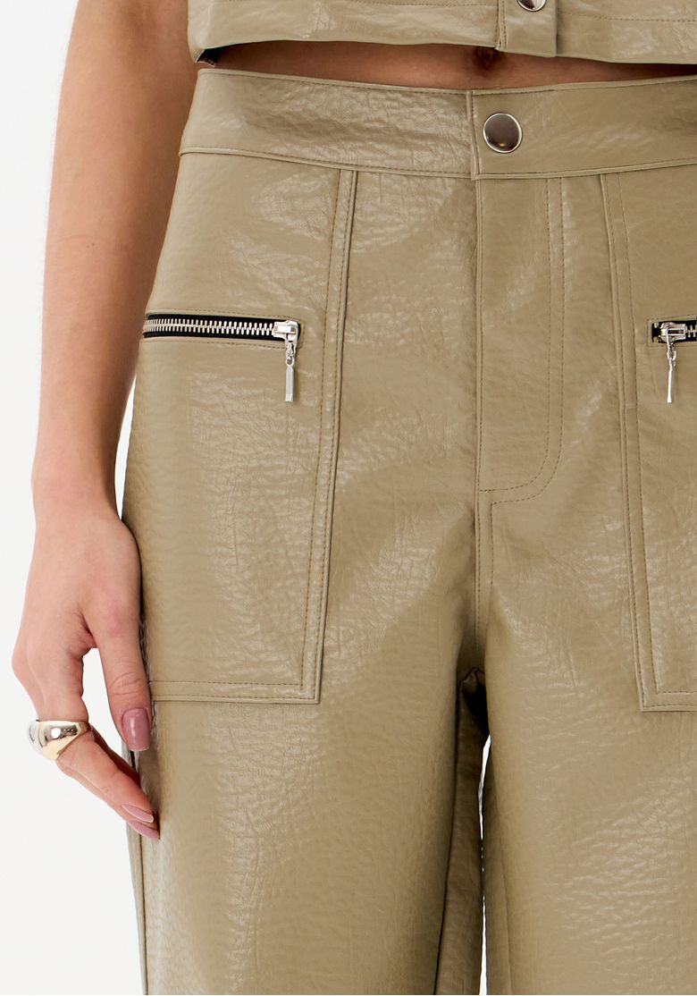 Detalhe dos bolsos frontais com zíper da calça em PU marrom.