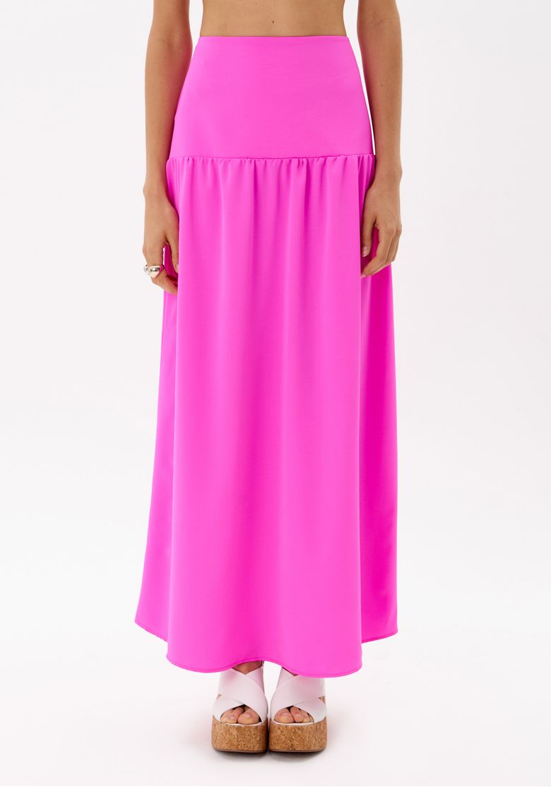 Vista traseira da modelo com saia super midi rosa e top peplum, mostrando caimento fluido do tecido e fechamento discreto nas costas