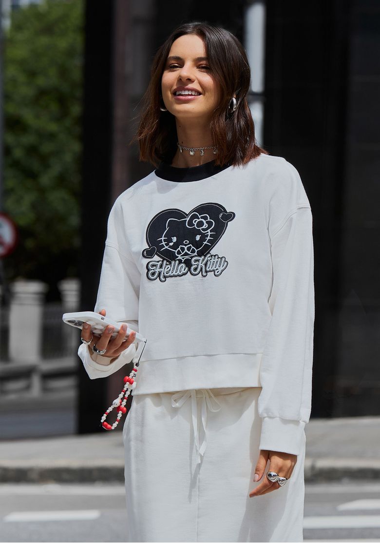 Mulher usando moletom feminino Hello Kitty branco com gola preta contrastante, mangas longas e estampa frontal em look casual urbano