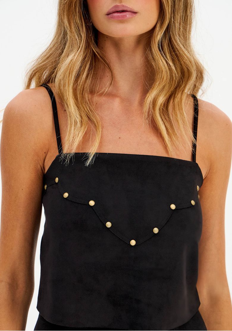 Detalhe do decote reto e das tachas douradas na blusa cropped camurça preta, acabamento aveludado.